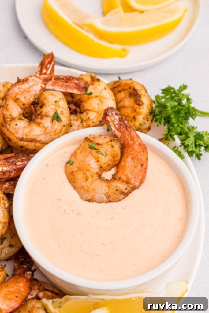 Crispy Air Fryer Shrimp 8 juicy cooked shrimp on a white plate with lemon wedges and a dipping sauce.