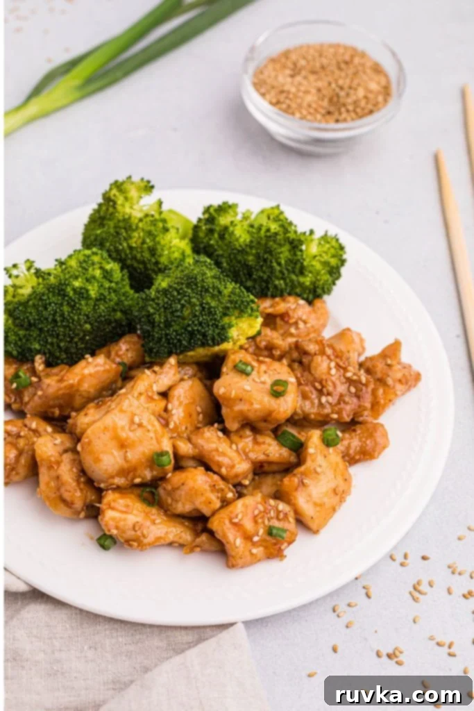 Crispy Air Fryer General Tso's Chicken 2 juicy chicken bites in sauce with sesame seeds and broccoli on a white plate.