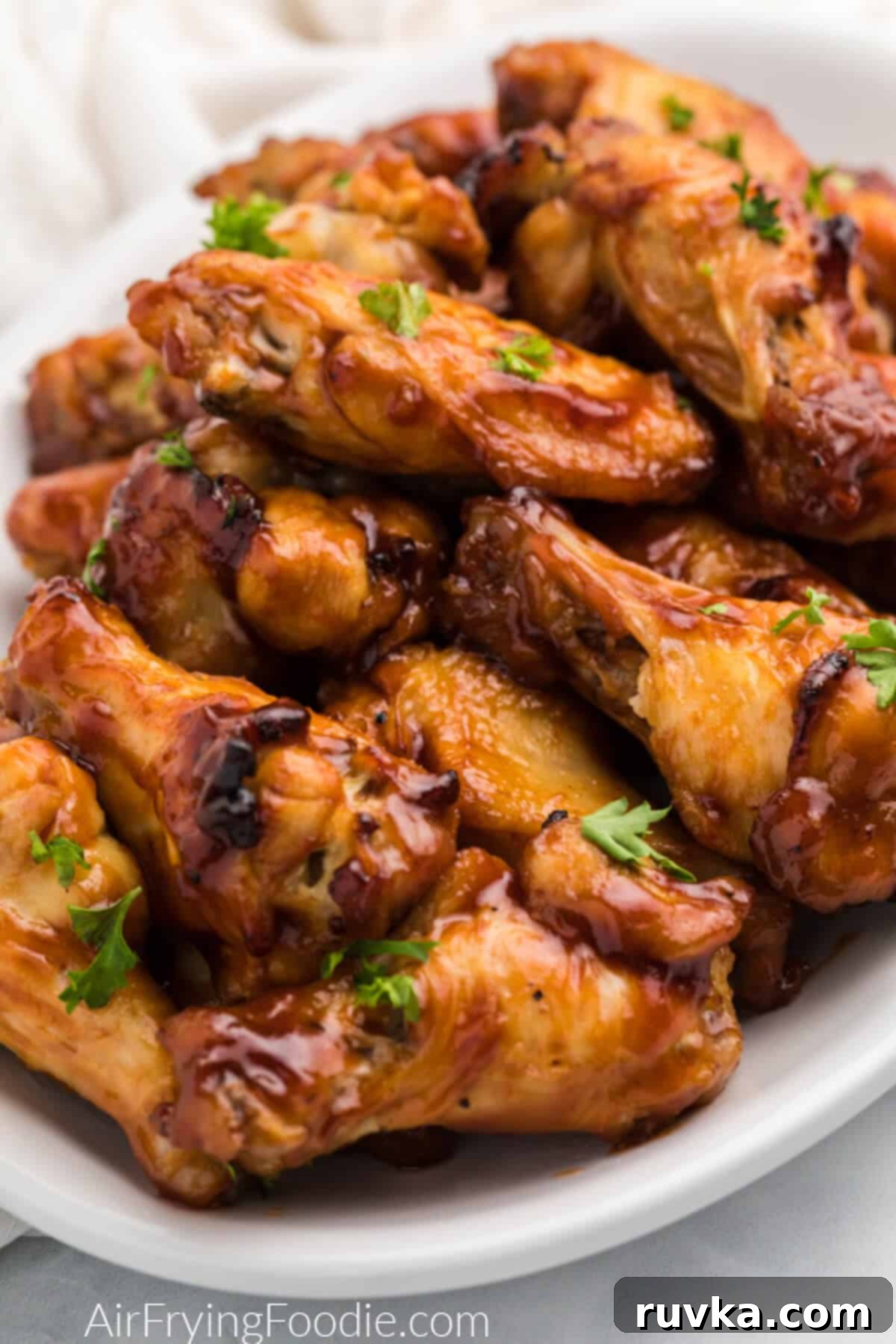 Crispy Air-Fried BBQ Wings 2 BBQ chicken wings made in the air fryer topped with fresh parsley and served on a white plate.