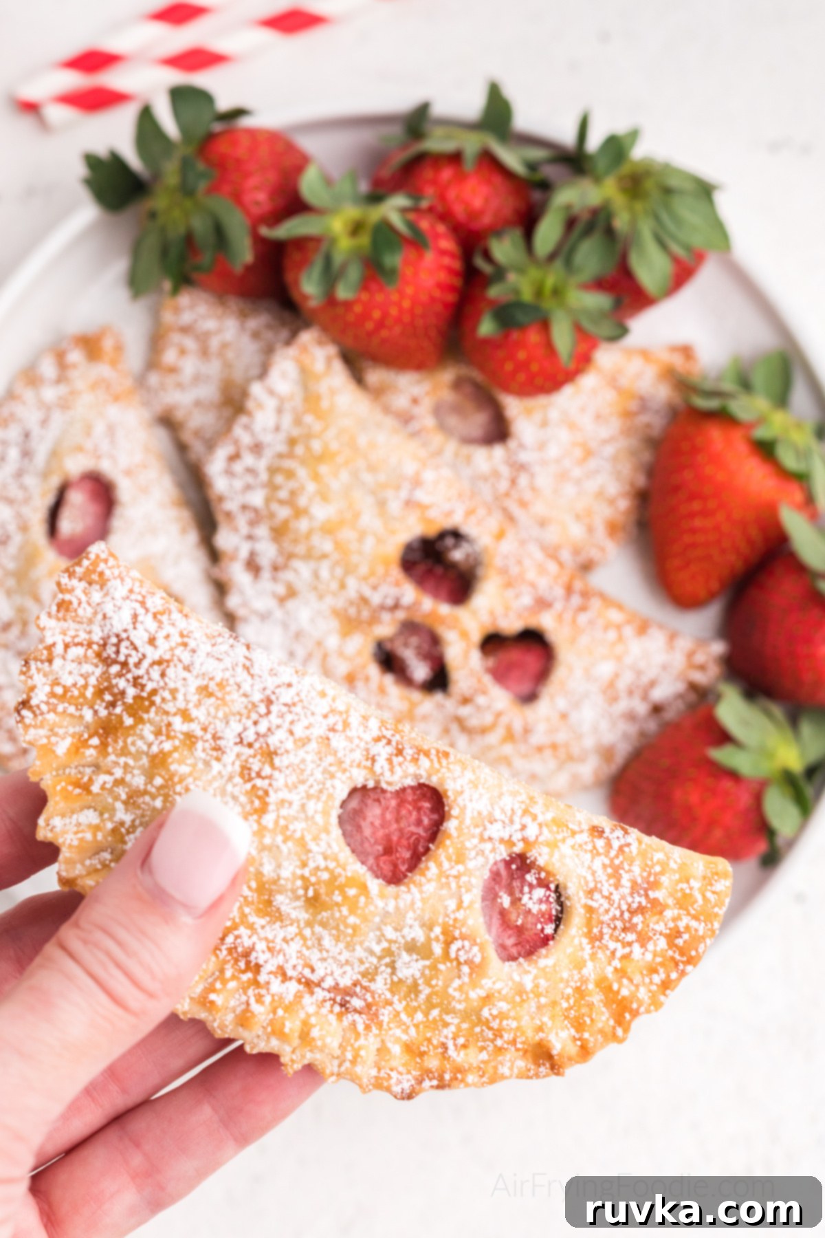 Easy Air Fryer Strawberry Nutella Hand Pies 2 Hand holding a golden-brown Air Fryer Strawberry Nutella Hand Pie dusted with powdered sugar, steam gently rising.