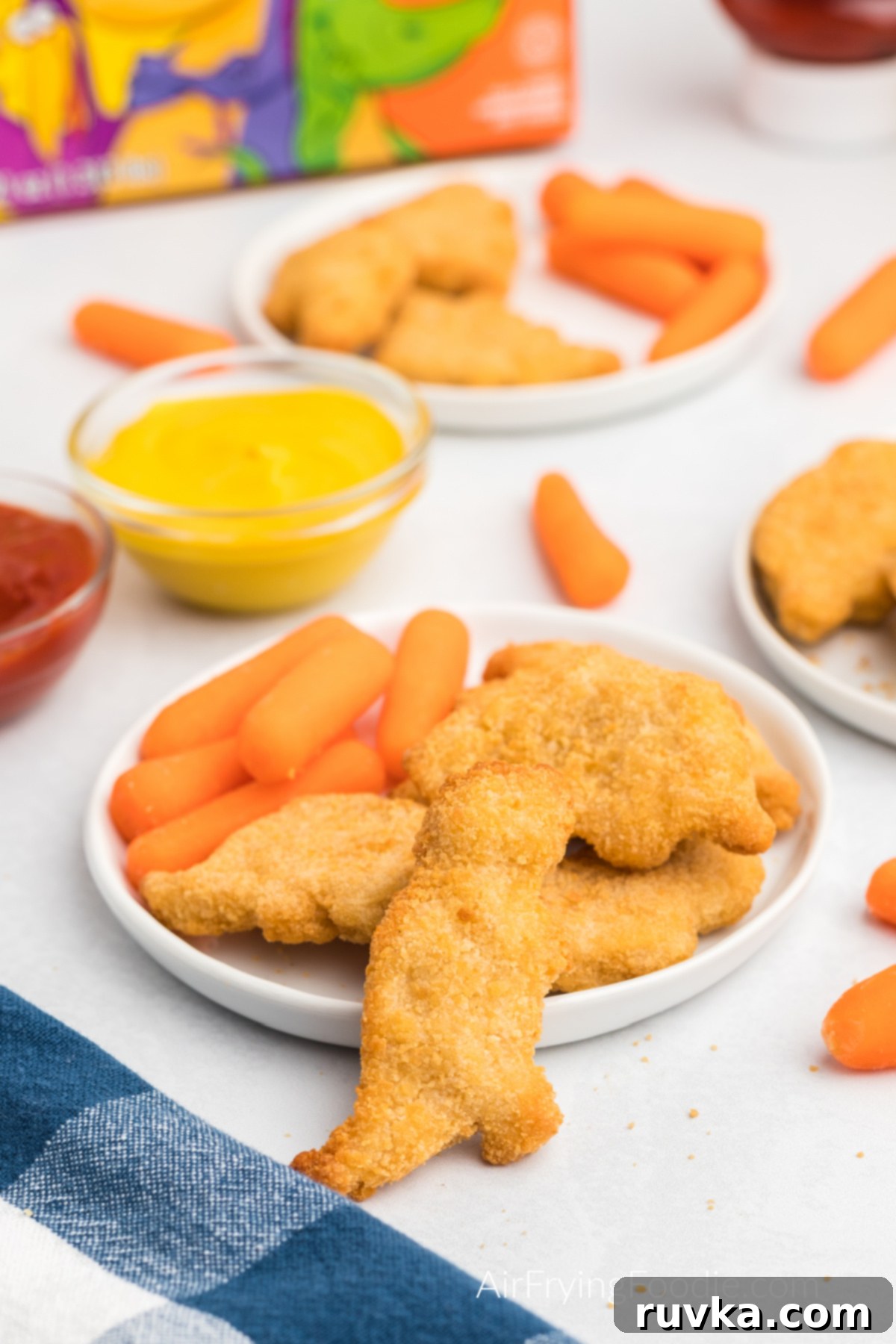 Crispy Air Fryer Dino Nuggets 6 Dino nuggets made in the air fryer and served on a white plate with a side of carrots.
