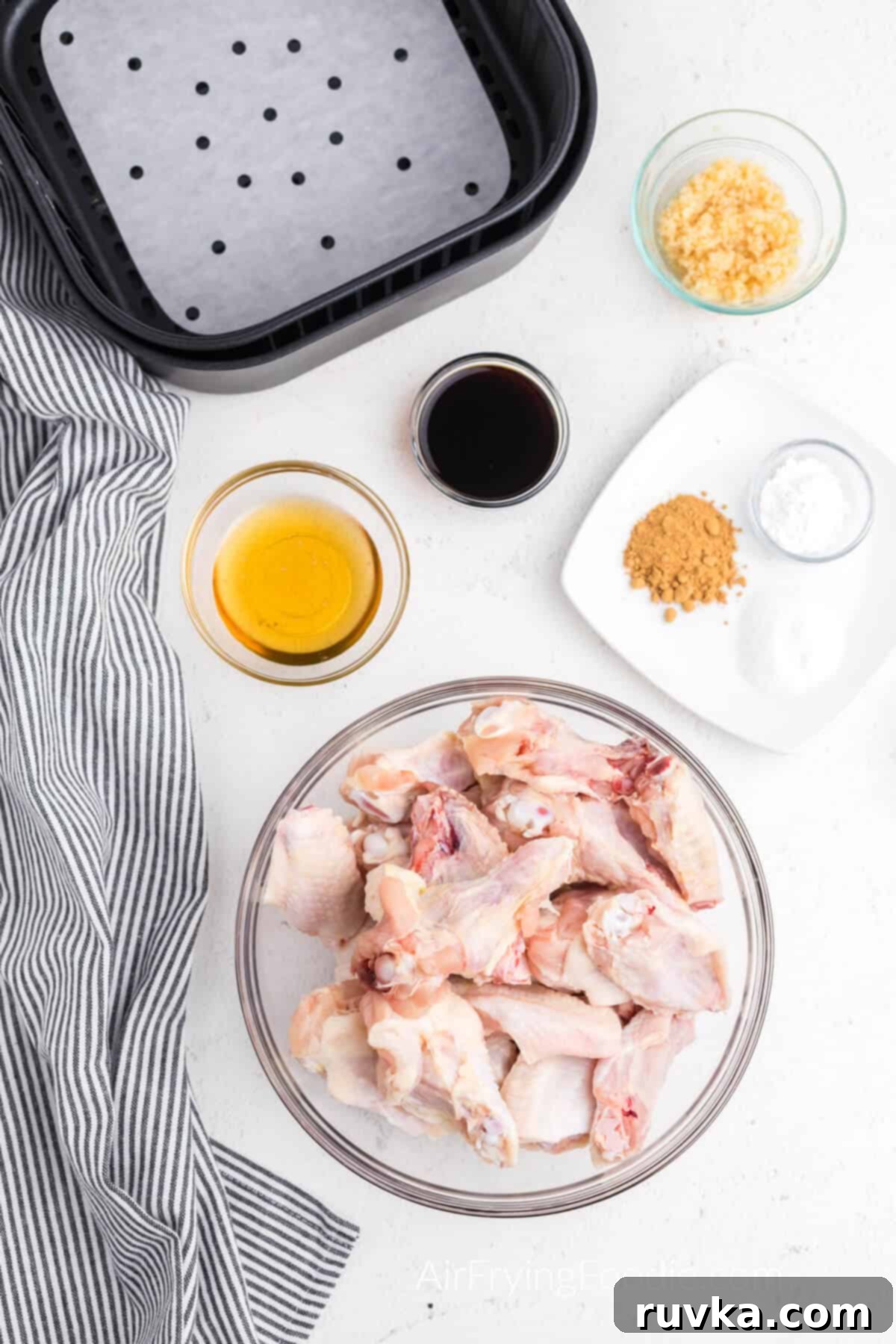Crispy Honey Garlic Air Fryer Wings 4 Chicken wings, honey, garlic, soy sauce, and other ingredients on a white plate next to a prepared air fryer basket.