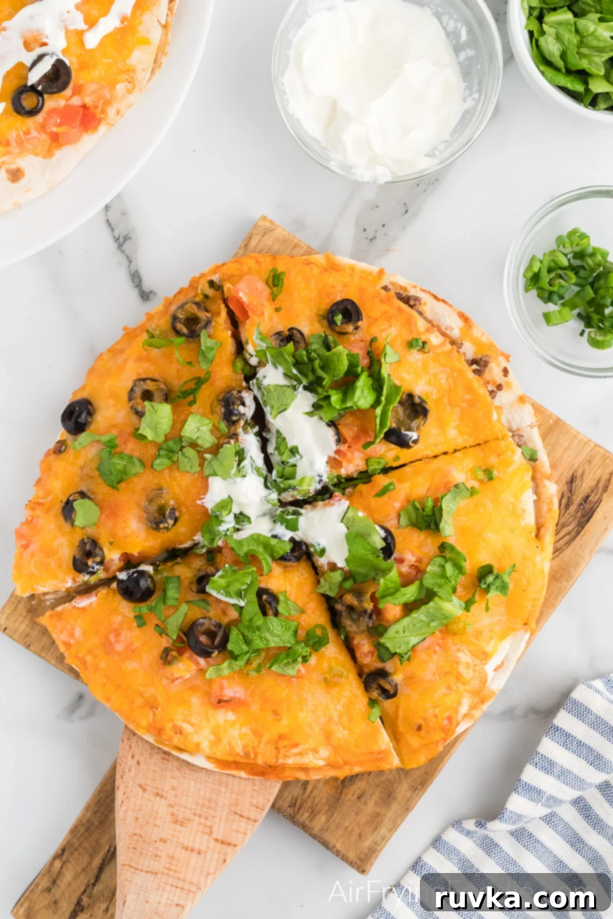Air Fryer Fiesta Pizza 11 Air Fryer Mexican Pizza Taco Bell copycat recipe on a board and topped with lettuce and sour cream and sliced and ready to serve.