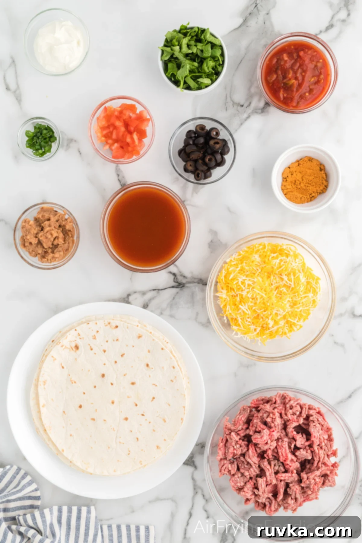 Air Fryer Fiesta Pizza 3 Ground beef, tortillas, cheese, sauce, beans, seasoning, lettuce, and more on a table to make mexican pizzas.