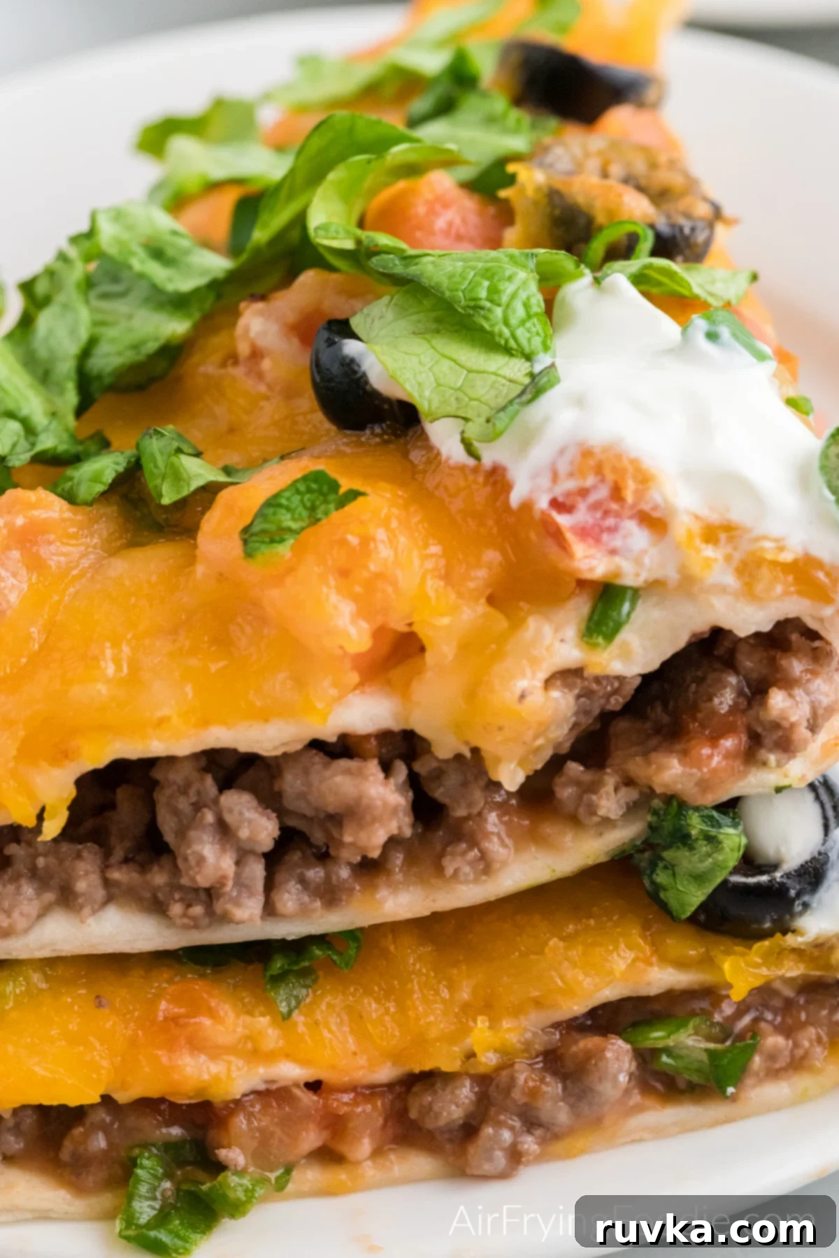 Air Fryer Fiesta Pizza 10 Close up of Mexican pizza sliced and stacked and toped with lettuce and sour cream.