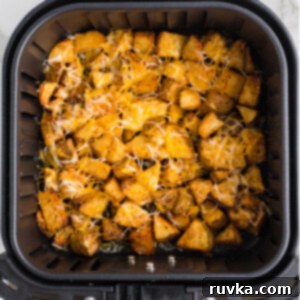 Crispy Cheesy Air Fryer Potatoes 12 Cheesy potatoes with perfectly melted cheese in the basket of an air fryer.