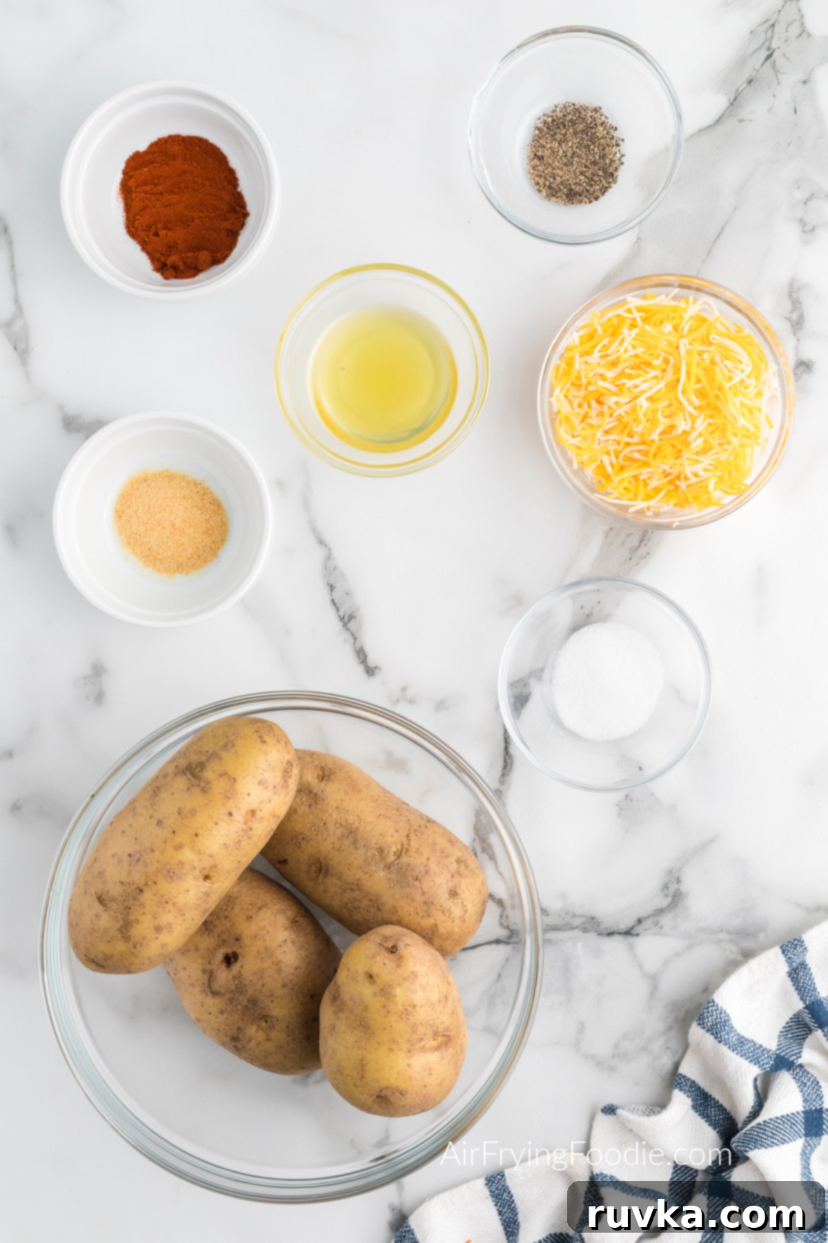 Crispy Cheesy Air Fryer Potatoes 3 A selection of fresh Russet potatoes, shredded cheddar jack cheese, olive oil, and various spices arranged on a surface, ready for making cheesy air fryer potatoes.