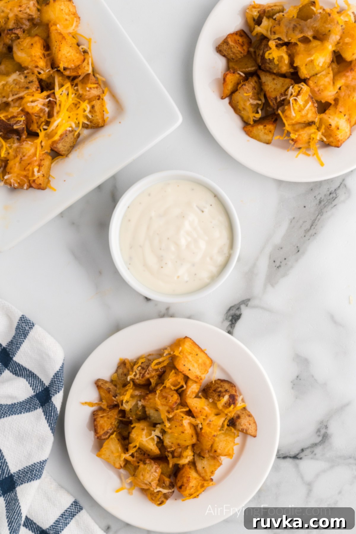 Crispy Cheesy Air Fryer Potatoes 9 A generous serving of air fryer cheesy potatoes, glistening with melted cheese, accompanied by a small bowl of creamy ranch for dipping.