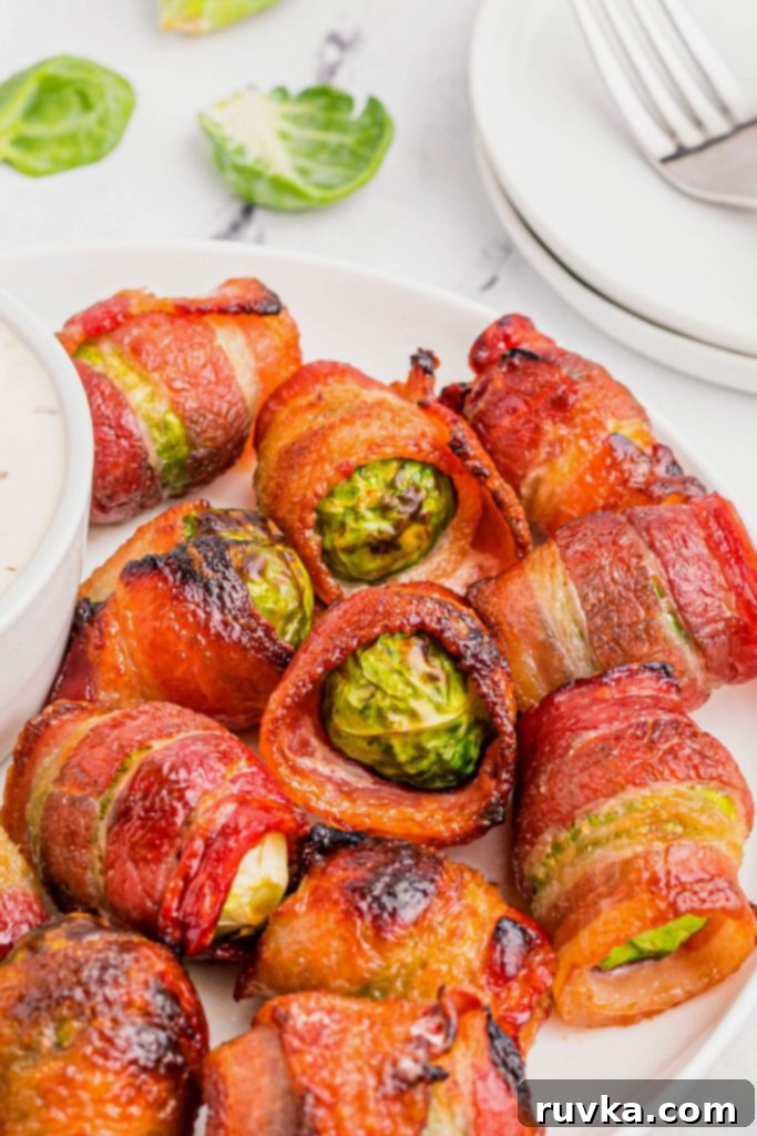 Crispy Air Fryer Bacon Brussels Bites 2 Golden juicy bacon wrapped brussels sprouts on a white plate with dipping sauce.