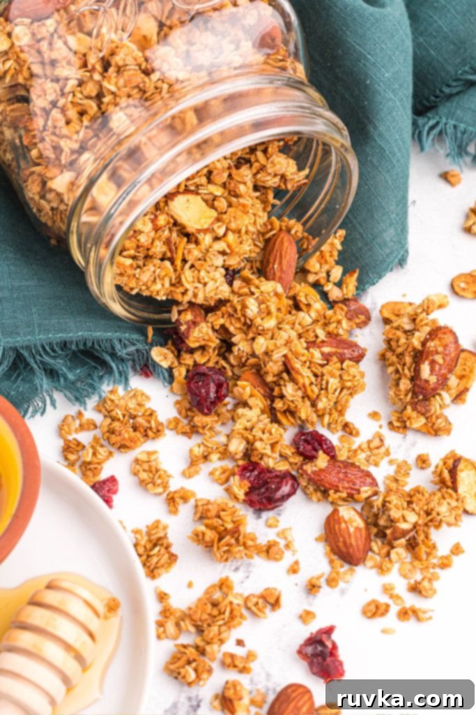 Easy Air Fryer Granola 2 Golden granola with nuts and dried fruit scattered on a white marble table with green linen