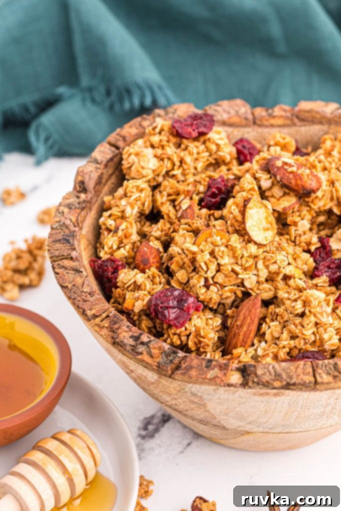 Easy Air Fryer Granola 7 Golden brown oats mixed with nuts and dried fruit in a wooden bowl on a marble table.