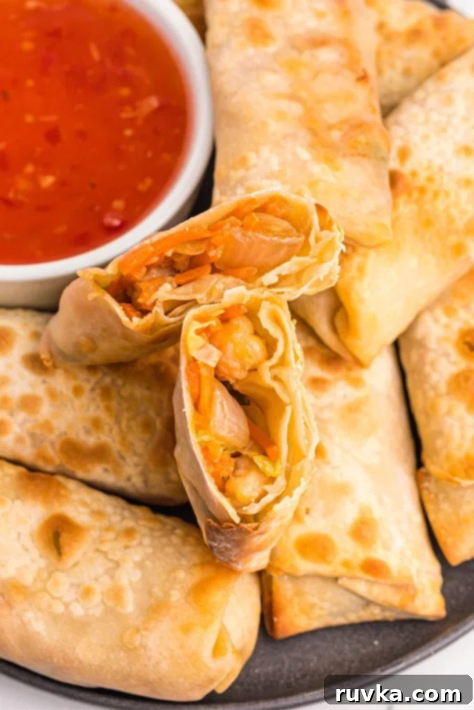 Crispy Air Fryer Shrimp Egg Rolls 2 Crispy shrimp egg rolls stacked on a white plate with dipping sauce.