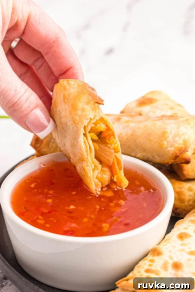 Crispy Air Fryer Shrimp Egg Rolls 9 Golden crispy egg roll being dipped into sweet and sour sauce