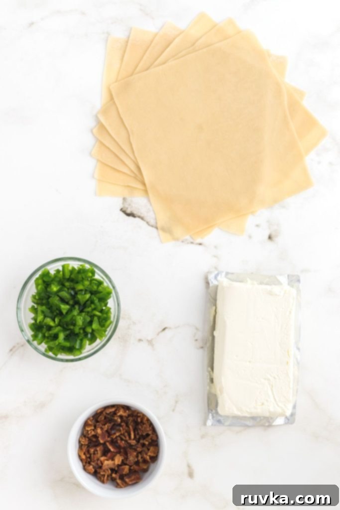 Air Fryer Jalapeno Popper Crunch Rolls 3 A selection of fresh bacon, chopped jalapenos, softened cream cheese, and egg roll wrappers neatly laid out on a marble countertop, ready for preparation.