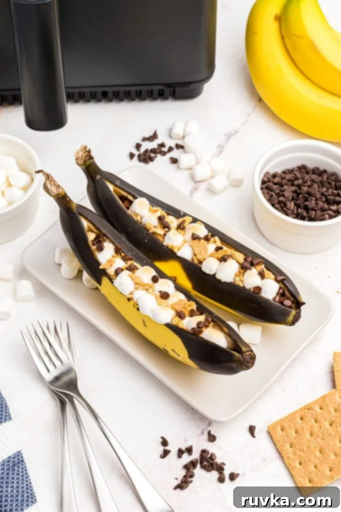 Air Fryer Golden Banana Delight 2 Bananas split open and filled with marshmallows and chocolate chips on a white plate, ready to be enjoyed as a dessert.