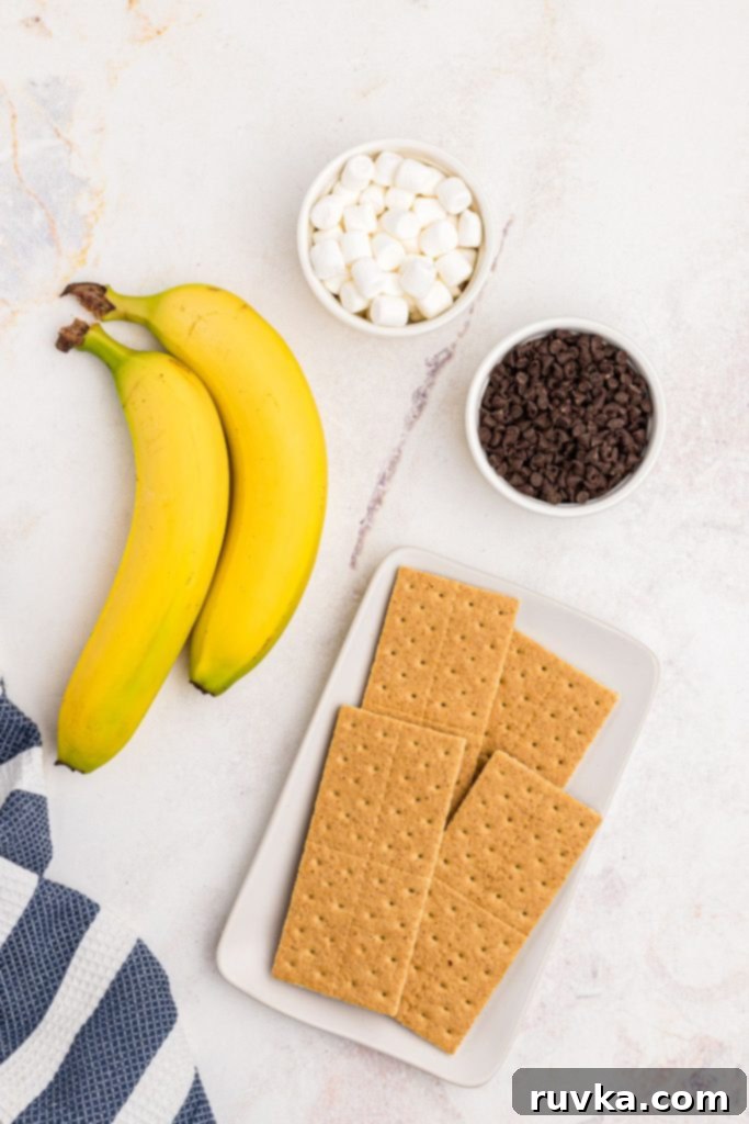 Air Fryer Golden Banana Delight 3 Graham crackers, bananas, mini chocolate chips, and mini marshmallows measured and arranged on a marble table, ready for assembly into banana boats.