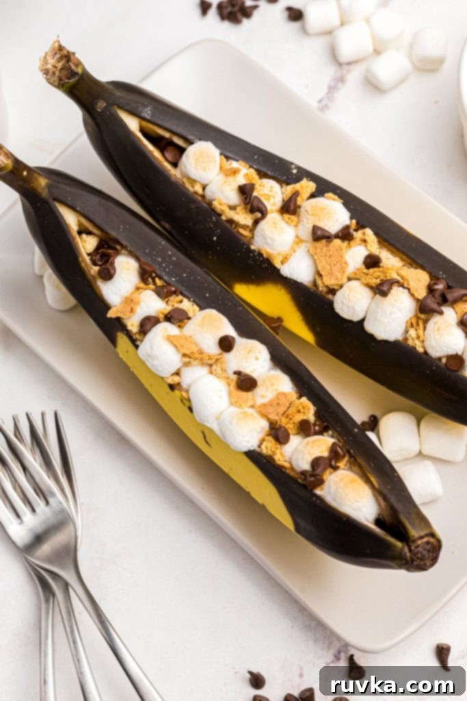 Air Fryer Golden Banana Delight 7 Bananas split open and filled with marshmallows and chocolate chips then topped with crumbled graham crackers, presented enticingly on a white plate.