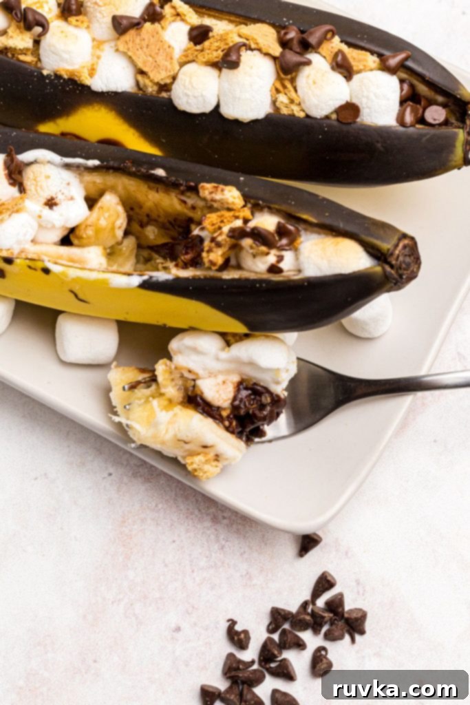 Air Fryer Golden Banana Delight 8 A fork holding a piece of melted chocolate and marshmallow with banana, in front of a perfectly stuffed and air-fried banana boat, highlighting the gooey deliciousness.