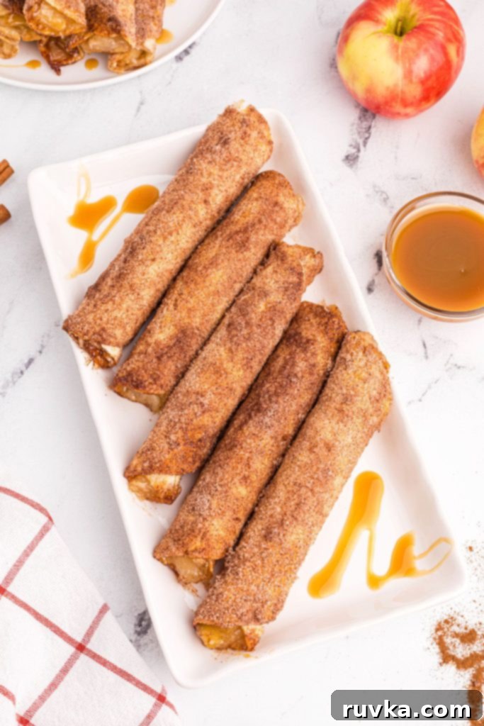 Crispy Air Fryer Apple Pie Taquitos 9 Golden sugar and cinnamon coated taquitos on a white plate with caramel drizzle sauce