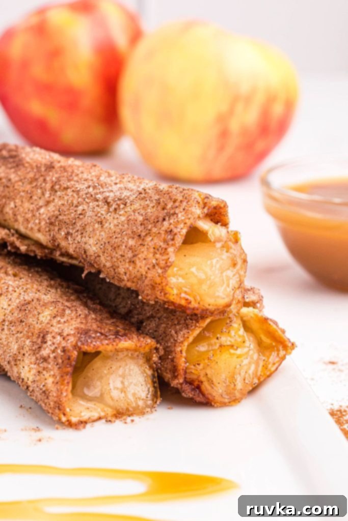 Crispy Air Fryer Apple Pie Taquitos 10 Golden crispy sugar and cinnamon coated taquitos stacked on a white plate with a caramel drizzle