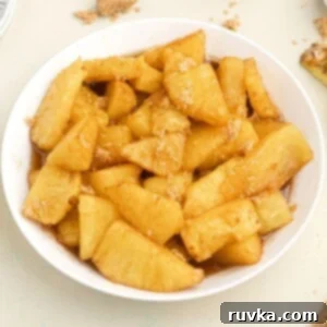 Air-Fried Caramelized Pineapple 7 Golden juicy pineapple bites, in juices, served in a white bowl, topped with sprinkled brown sugar.