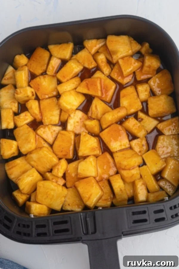 Air-Fried Caramelized Pineapple 4 Uncooked pineapple pieces, covered in melted butter, sugars, and cinnamon, in an air fryer basket.