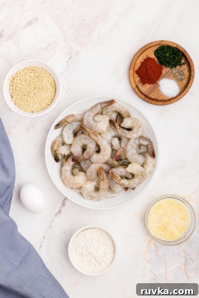 Crispy Air Fryer Breaded Shrimp 3 Uncooked shrimp in a white bowl surrounded by breadcrumbs, flour, egg, parm cheese, and seasonings.