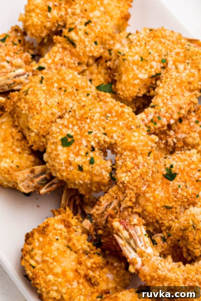Crispy Air Fryer Breaded Shrimp 10 Golden breaded shrimp stacked on a white plate.