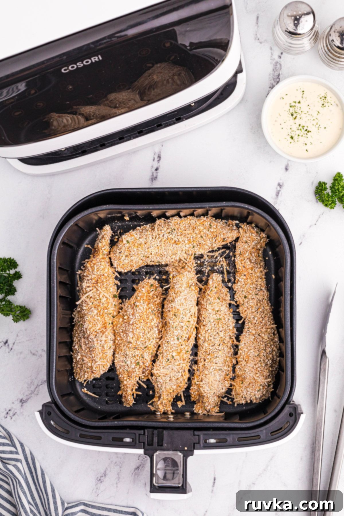 Crispy Golden Oat Air Fryer Chicken 6 Uncooked coated chicken in an air fryer basket on a white marble table.