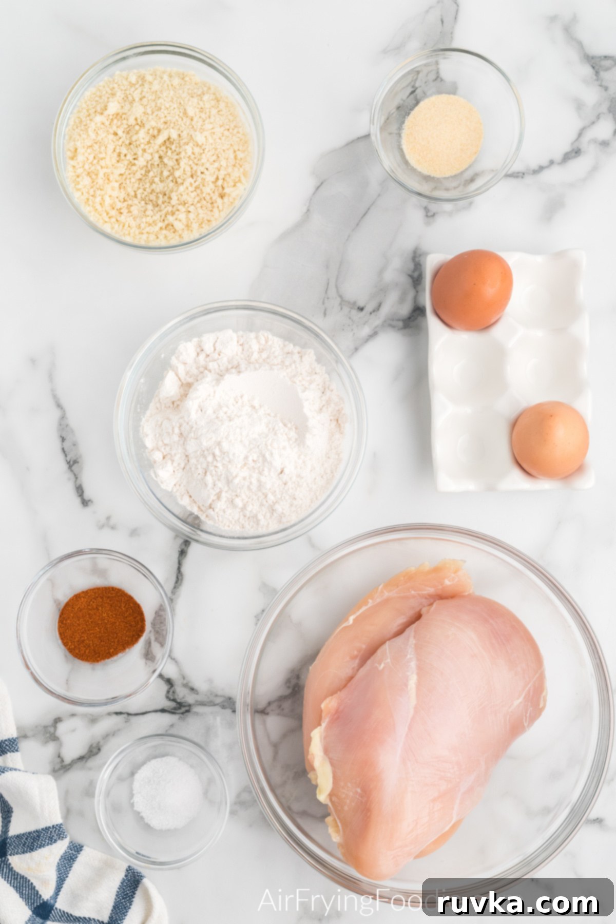 Crispy Air Fryer Boneless Wings 3 chicken breast, flour, seasoning, eggs, and breadcrumbs on a white table to make boneless chicken wings.