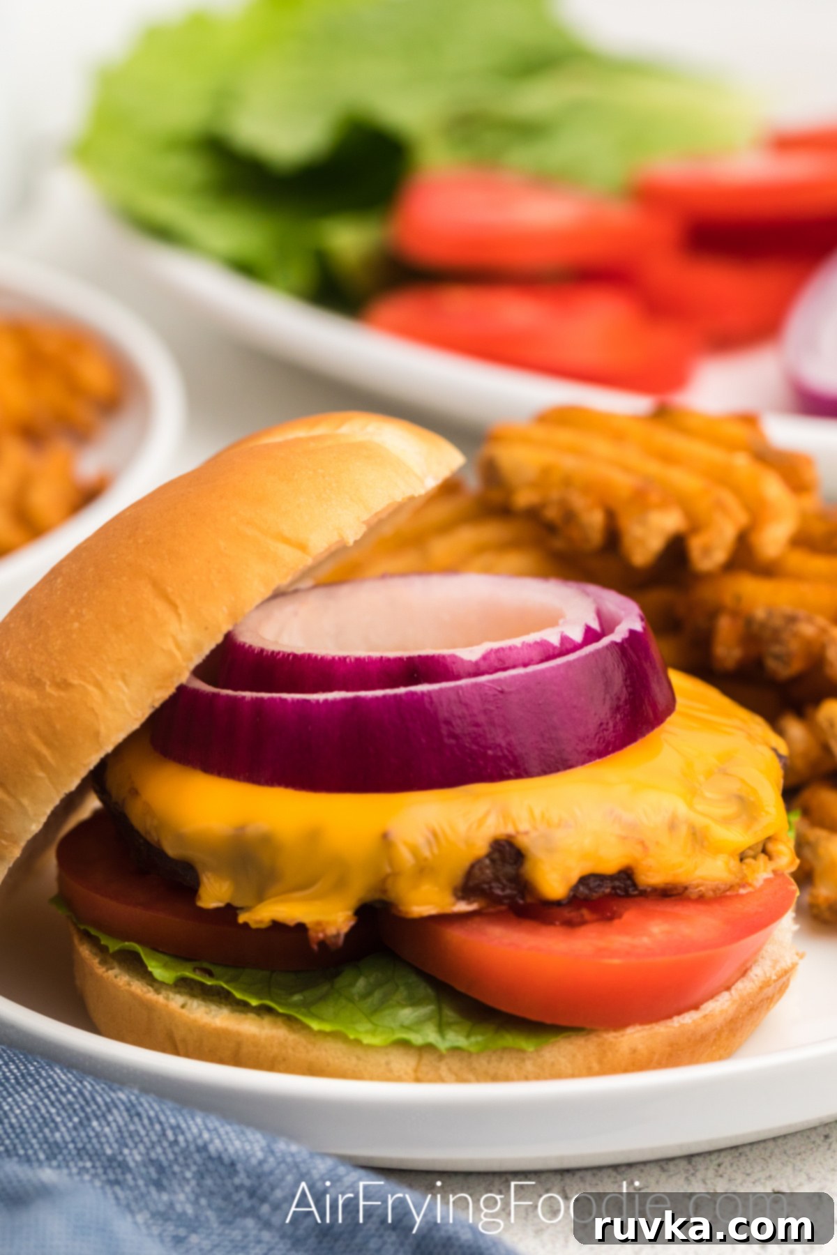 Perfect Air Fryer Frozen Burgers 2 Air fried frozen burger topped with cheese, onions, tomatoes, and lettuce, and served with a side of waffle fries.