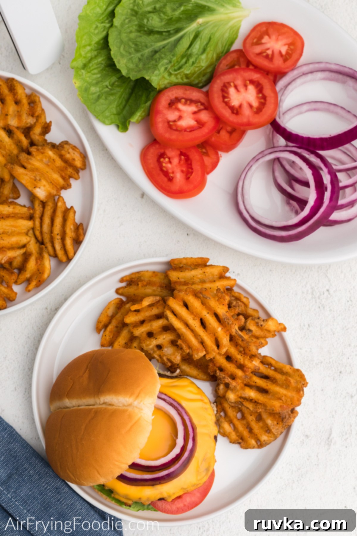 Perfect Air Fryer Frozen Burgers 6 Air fried burger with cheese and topped with onion on a plate with waffle fries.