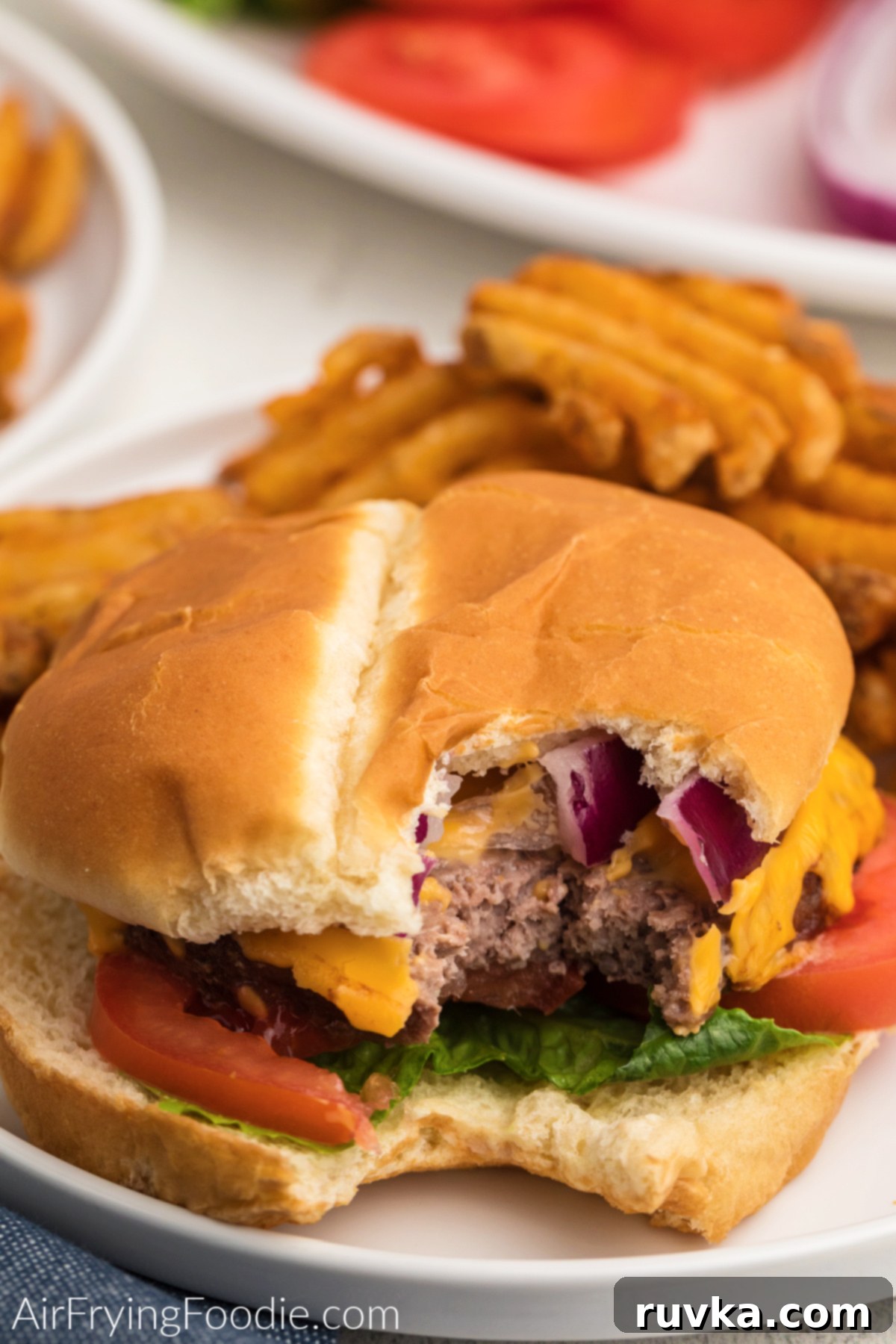 Perfect Air Fryer Frozen Burgers 7 Dressed air fried burger with a bite missing, on a plate with waffle fries.