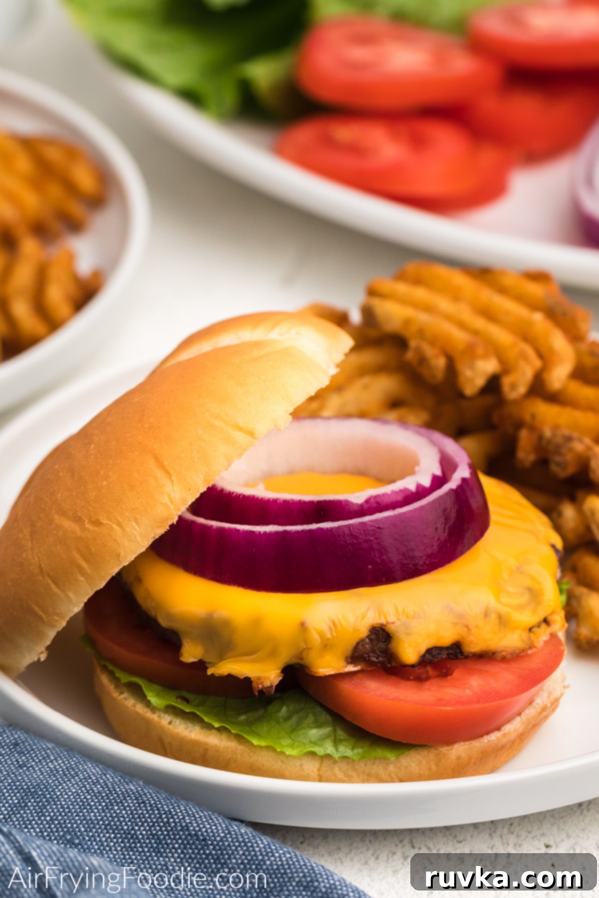 Perfect Air Fryer Frozen Burgers 8 Air fried frozen burger topped with cheese, onion, tomato, and lettuce, and served on a plate with waffle fries.