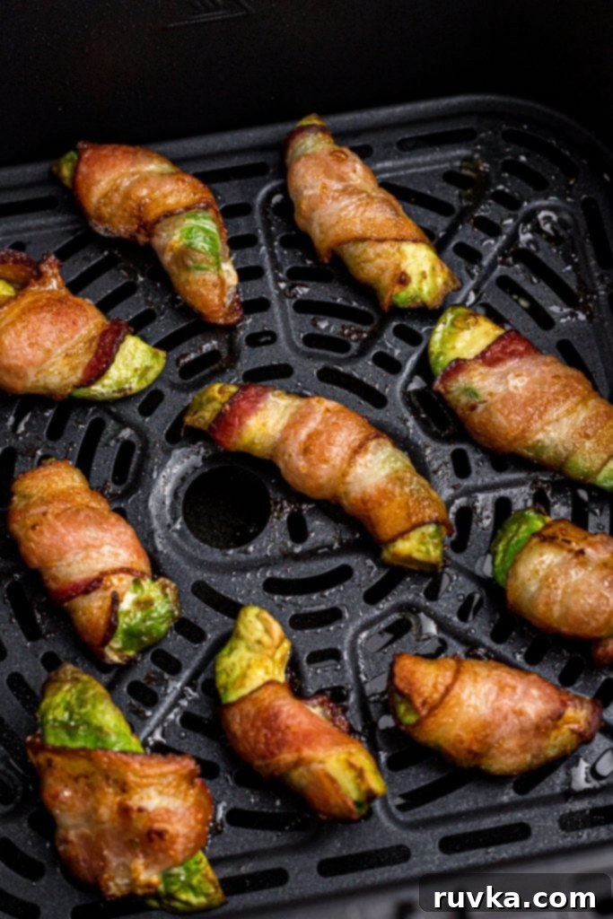 Air Fryer Bacon Wrapped Avocado Perfection 8 Crispy juicy bacon wrapped around avocado wedges in the air fryer basket after being cooked.