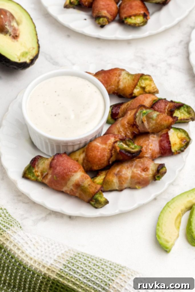 Air Fryer Bacon Wrapped Avocado Perfection 9 Crispy bacon wrapped around avocado wedges on a white plate with ranch dressing