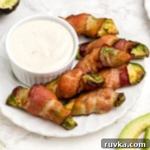Air Fryer Bacon Wrapped Avocado Perfection 10 Crispy bacon wrapped around avocado wedges on a white plate