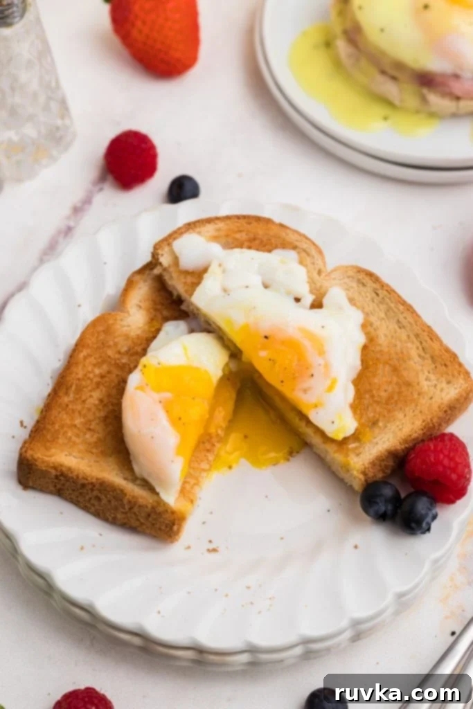 Perfect Air Fryer Poached Eggs 2 Poached egg on a piece of toast on a white plate with berries in front of a plate with eggs benedict.
