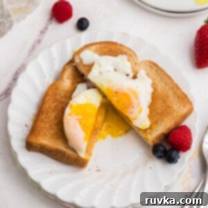 Perfect Air Fryer Poached Eggs 9 Poached egg on toast cut in half with yolk spilling out. Fresh fruit as a garnish on a white plate.