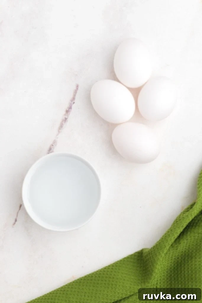 Perfect Air Fryer Poached Eggs 3 Four eggs and a ramekin of water on the marble table.