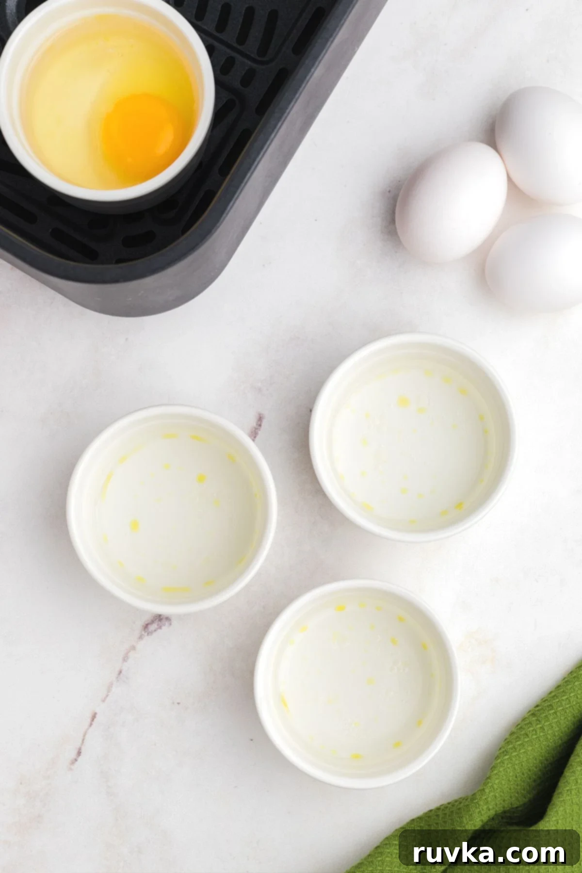 Perfect Air Fryer Poached Eggs 4 Sprayed ramekins being filled with water and egg and placed in the air fryer basket.