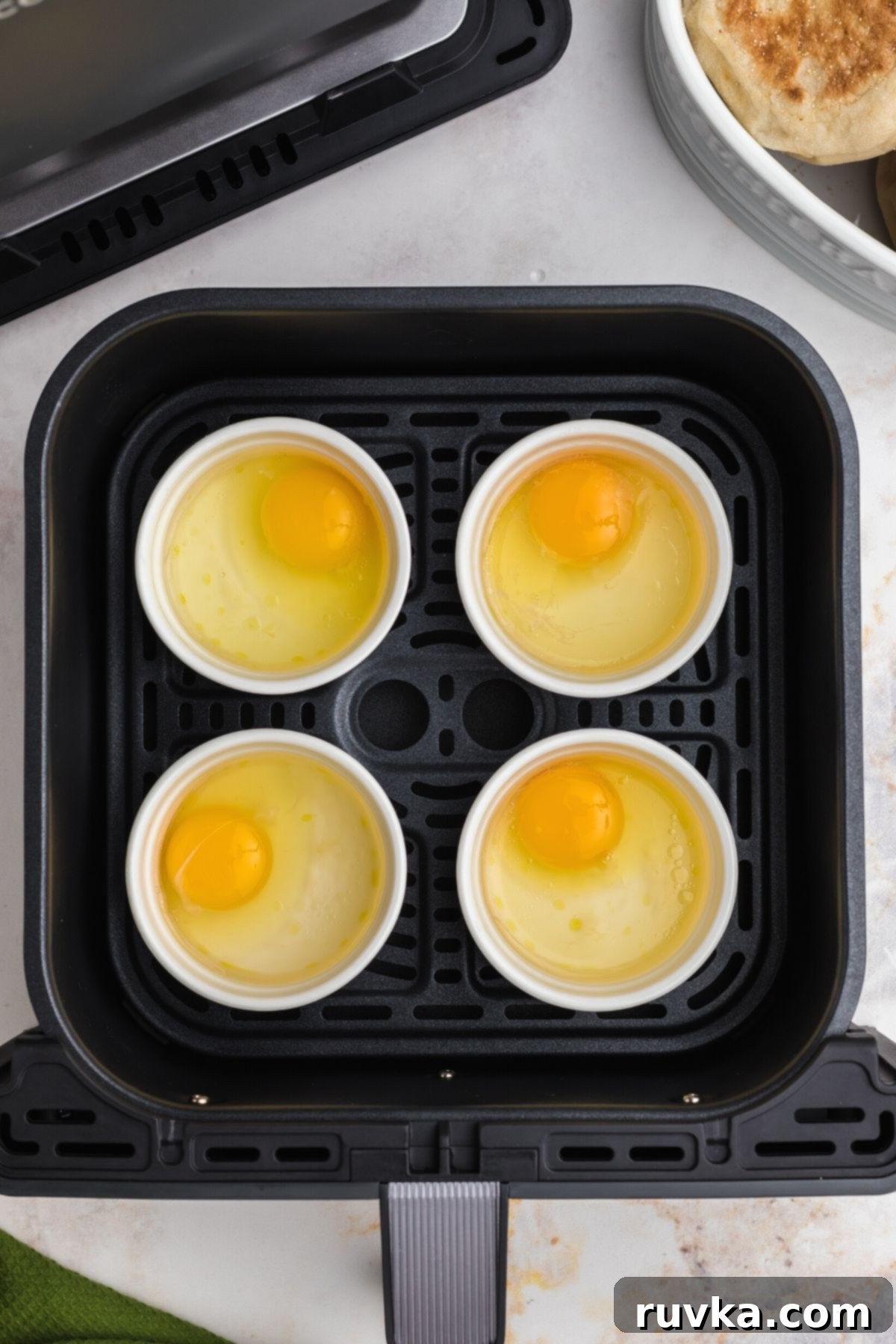 Perfect Air Fryer Poached Eggs 5 Uncooked eggs in ramekins filled with water in the air fryer basket.