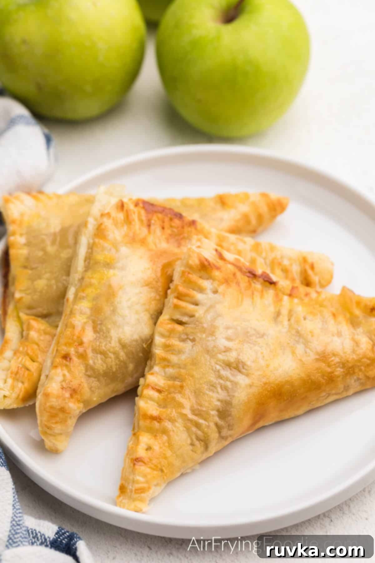 Crispy Air Fryer Apple Turnovers 2 Air fryer apple turnovers served on a white plate, garnished with a light dusting of powdered sugar.
