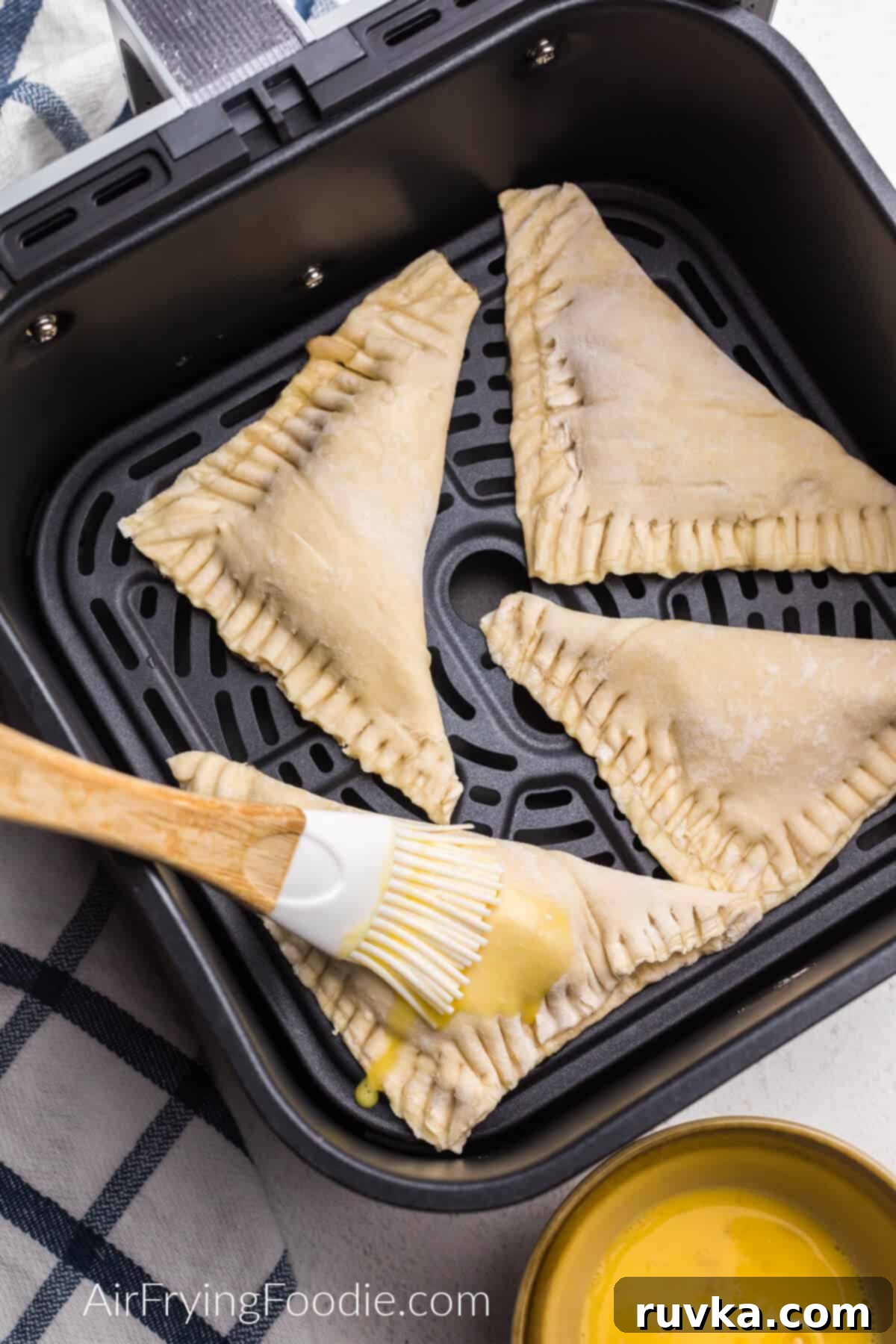 Crispy Air Fryer Apple Turnovers 5 Apple turnovers in the air fryer basket being brushed with egg before frying.