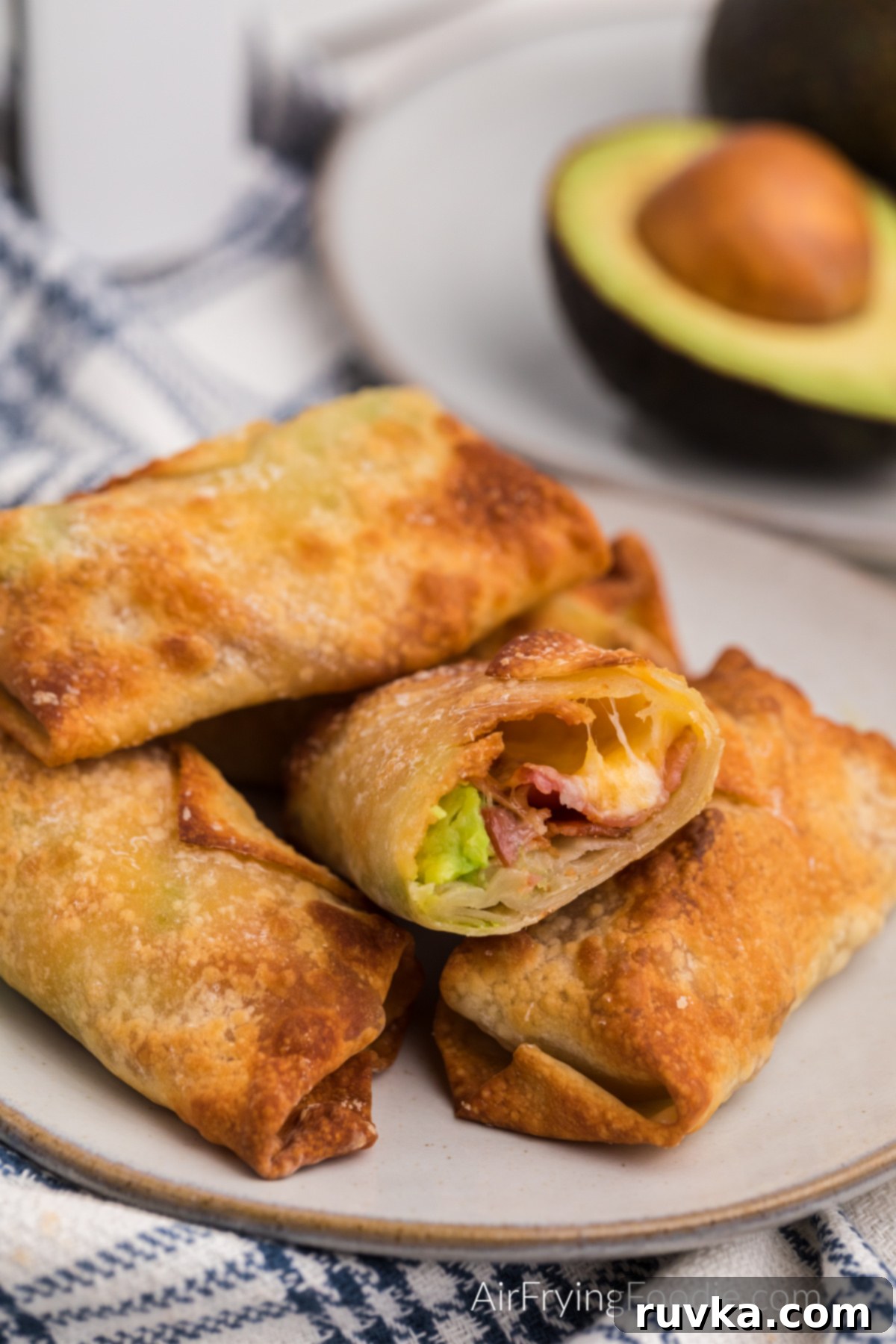 Crispy Air Fryer Avocado Bacon Egg Rolls 2 Crispy Air Fried Avocado Bacon Egg Rolls stacked on a plate, one with a savory bite missing, showcasing the delicious filling.