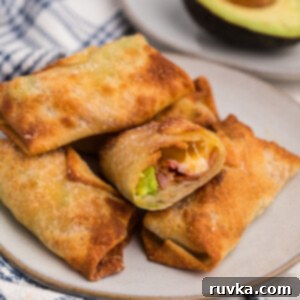 Crispy Air Fryer Avocado Bacon Egg Rolls 12 Crispy Air Fryer Avocado Bacon Egg Rolls stacked on a plate with one missing a bite, showing the creamy filling.