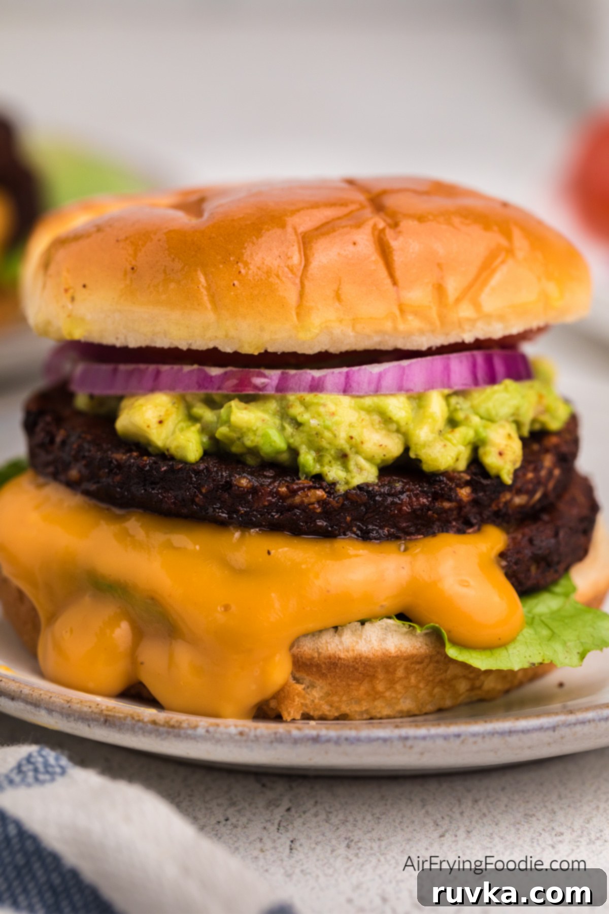 Crispy Air Fryer Black Bean Burger 8 Air fried black bean burger with mashed avocado, sauce, lettuce, onion, and tomato on a bun.