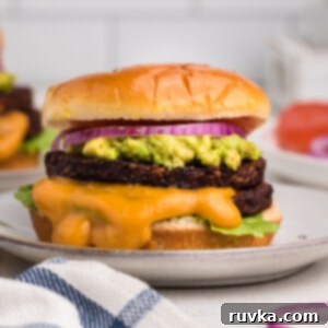 Crispy Air Fryer Black Bean Burger 9 Close up photo of a black bean burger made in the air fryer and topped with mashed avocado, onion, sauce, and a bun.