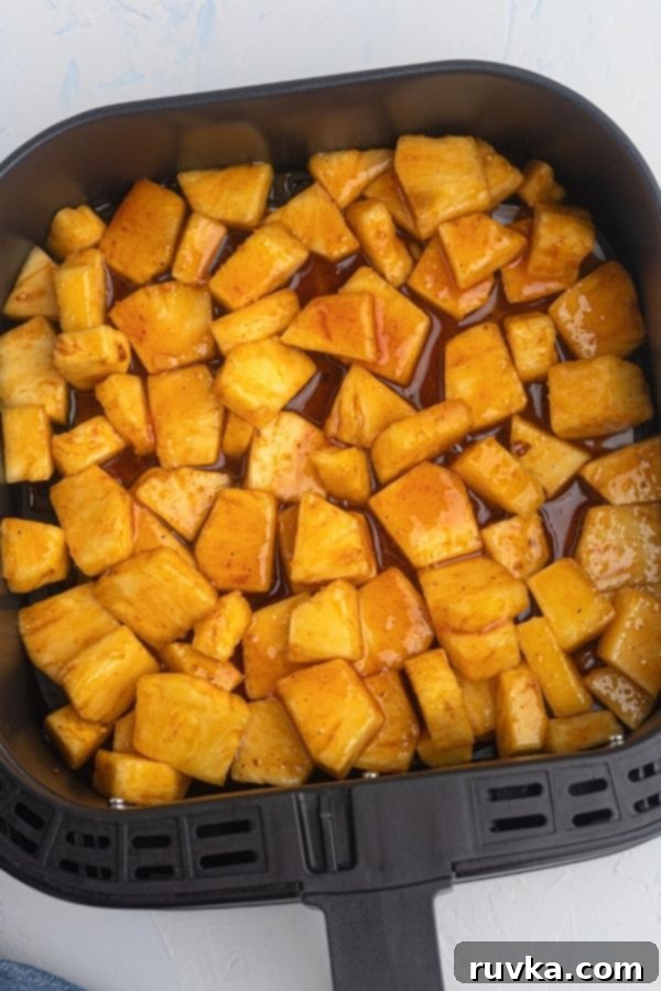 Air Fried Honey BBQ Pineapple 4 Juicy golden pineapple chunks coated in honey and bbq glaze, arranged in an air fryer basket, ready to be cooked.