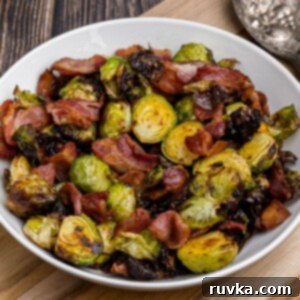 Crispy Air Fryer Brussels Sprouts and Bacon 11 Crispy green brussels sprouts and bacon strips in a white bowl on a wooden cutting board.